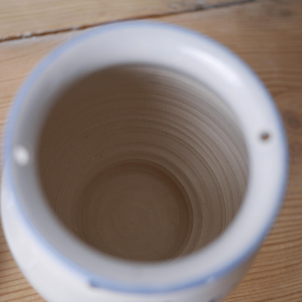 Top-down view of an empty white mug with a blue rim on a wooden table, showing the mug's inner ridged interior.