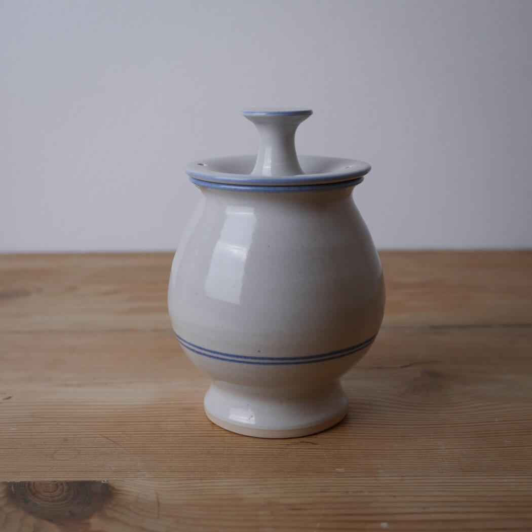 Gray ceramic vase with a lid and blue trim on a wooden table surface.