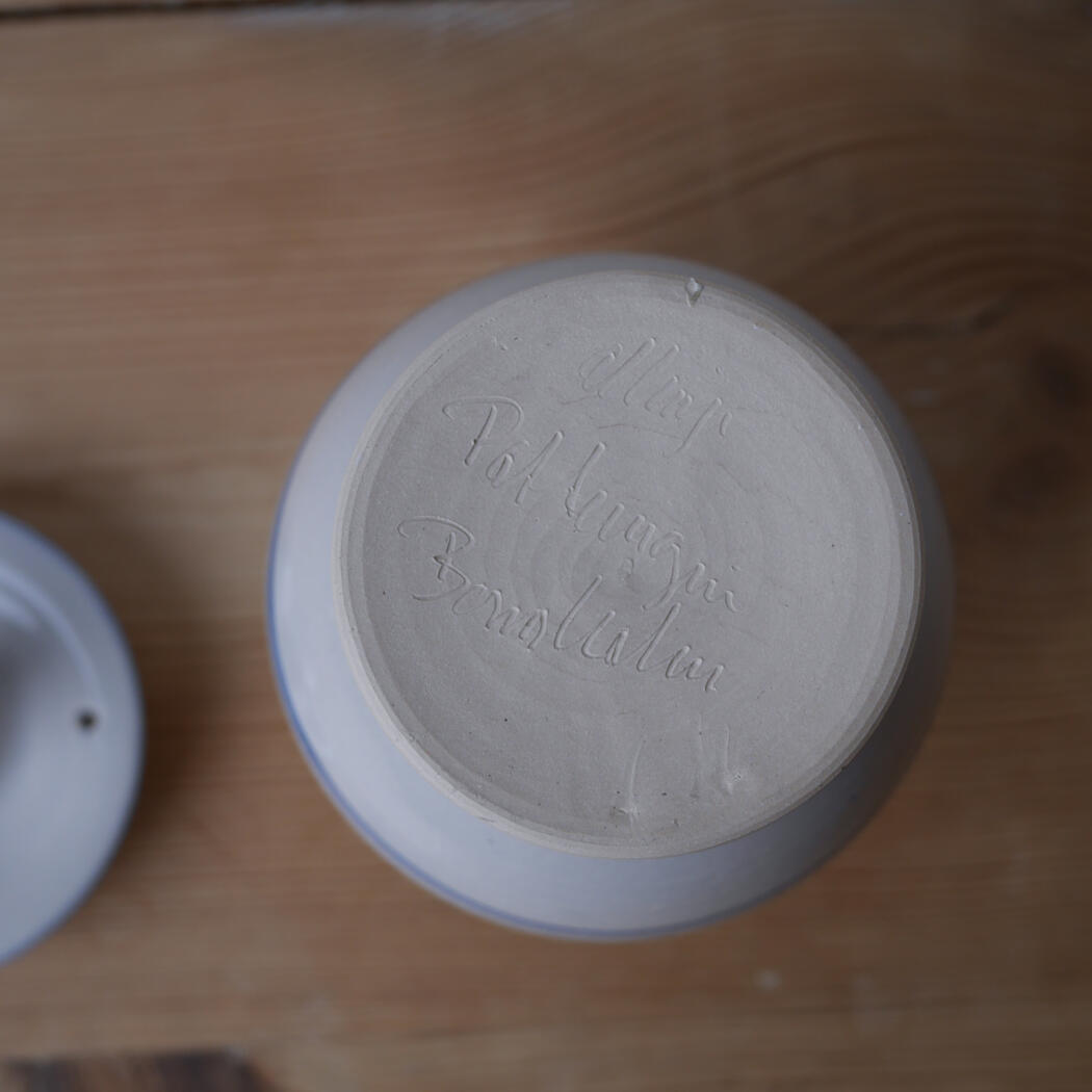 Bottom view of a pale blue ceramic bowl showing an unglazed base with a cursive inscription (text difficult to read).