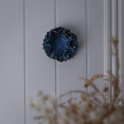 Blue scalloped ceramic wall decor mounted on a white paneled wall with dried plants in the foreground.