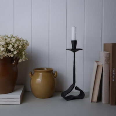 Rustic still-life on a shelf: brown ceramic vase with white flowers, a yellow pot, a black iron candlestick, and books.