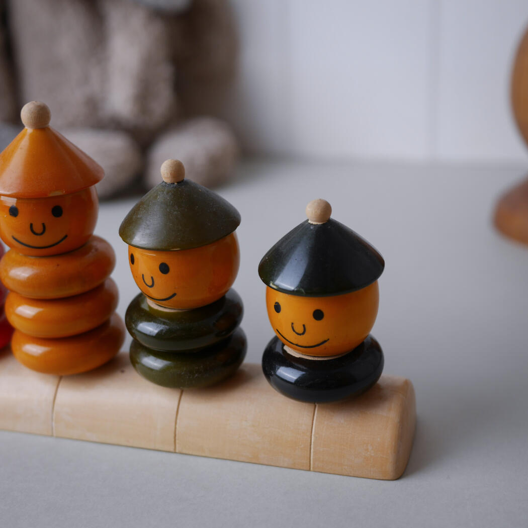 Three smiling wooden stacker figurines with cone hats on a light wooden track.