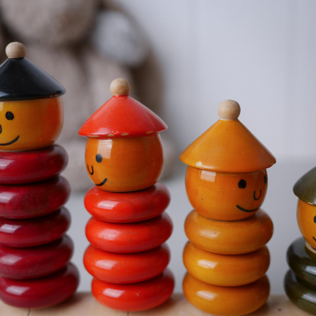 Smiling wooden stackable toys in red, orange, and yellow with cone hats lined up on a table.