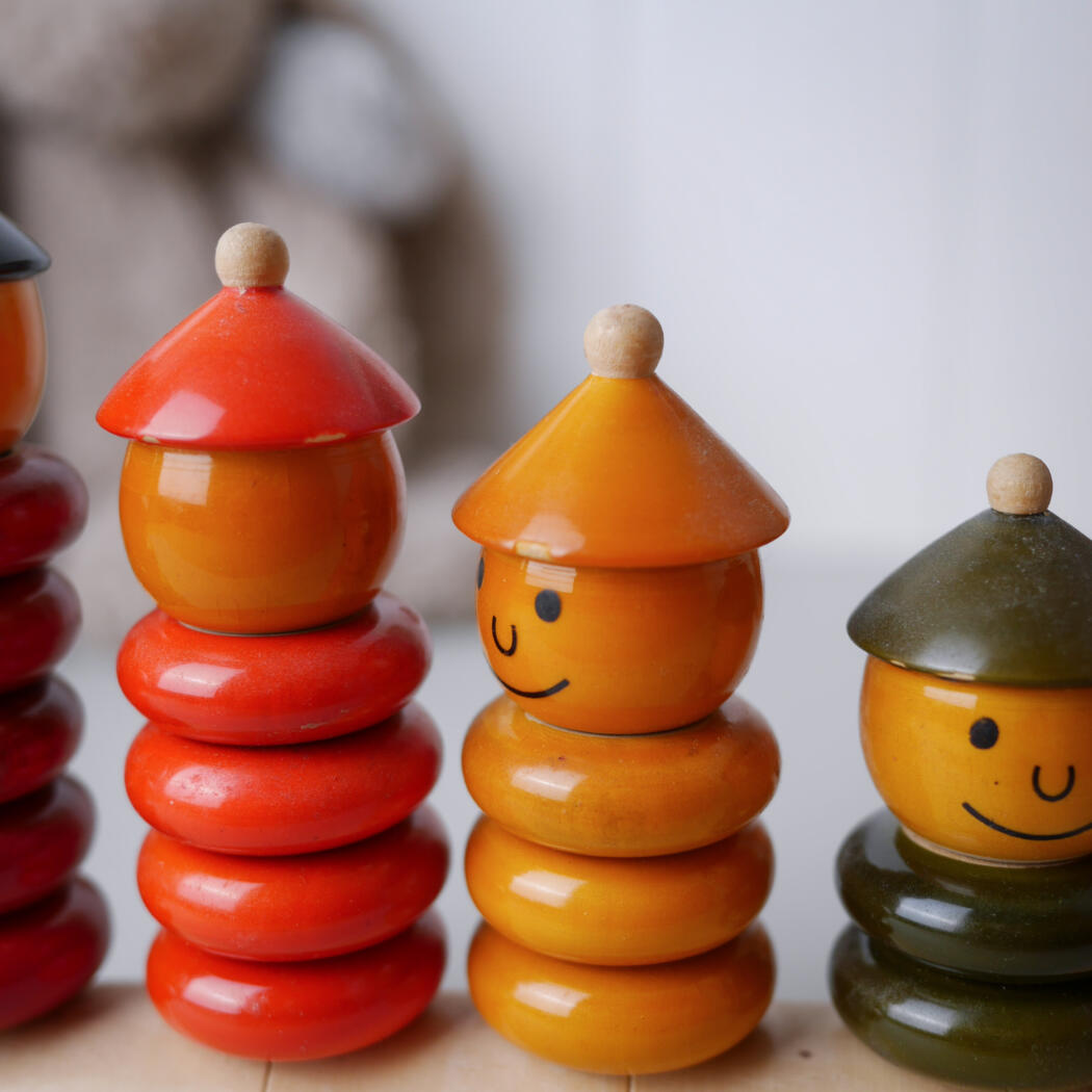 Colorful wooden stacking toys with smiling faces arranged in a row on a light surface.