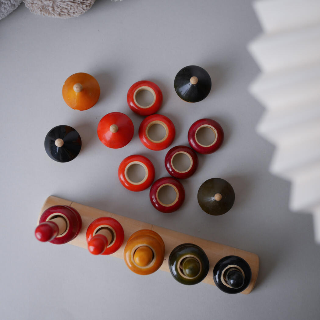 Top-down view of a wooden stacking toy with red, orange, and black round pieces on a light gray surface.