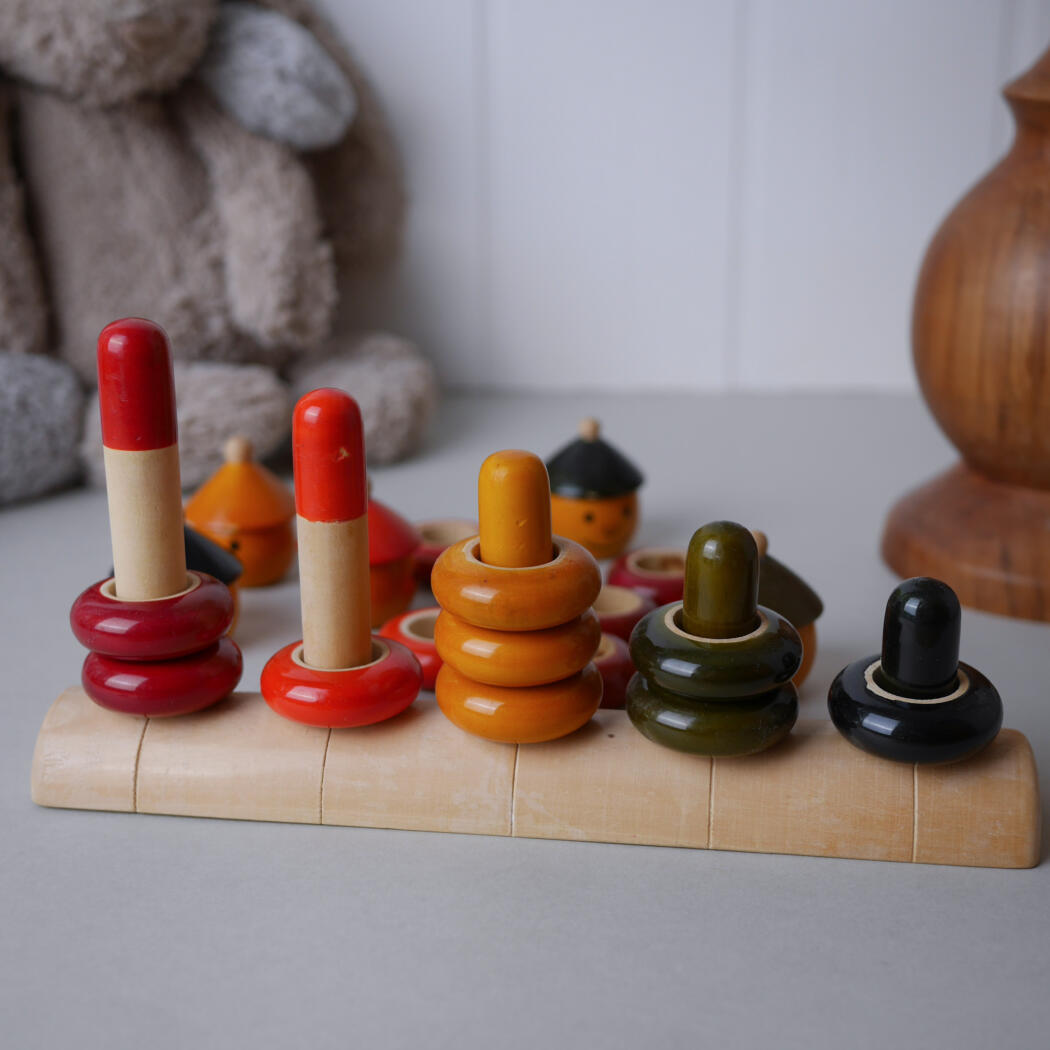 Wooden ring-stacking toy with colored rings on vertical pegs atop a light wooden base.
