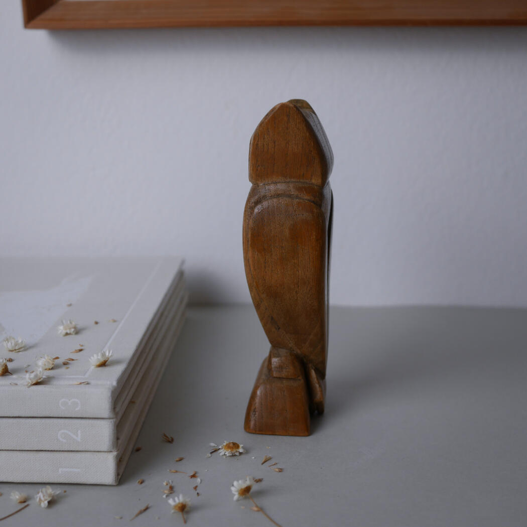 Wooden carved humanoid figure standing upright beside a stack of white numbered books, with small white flowers scattered on the desk.