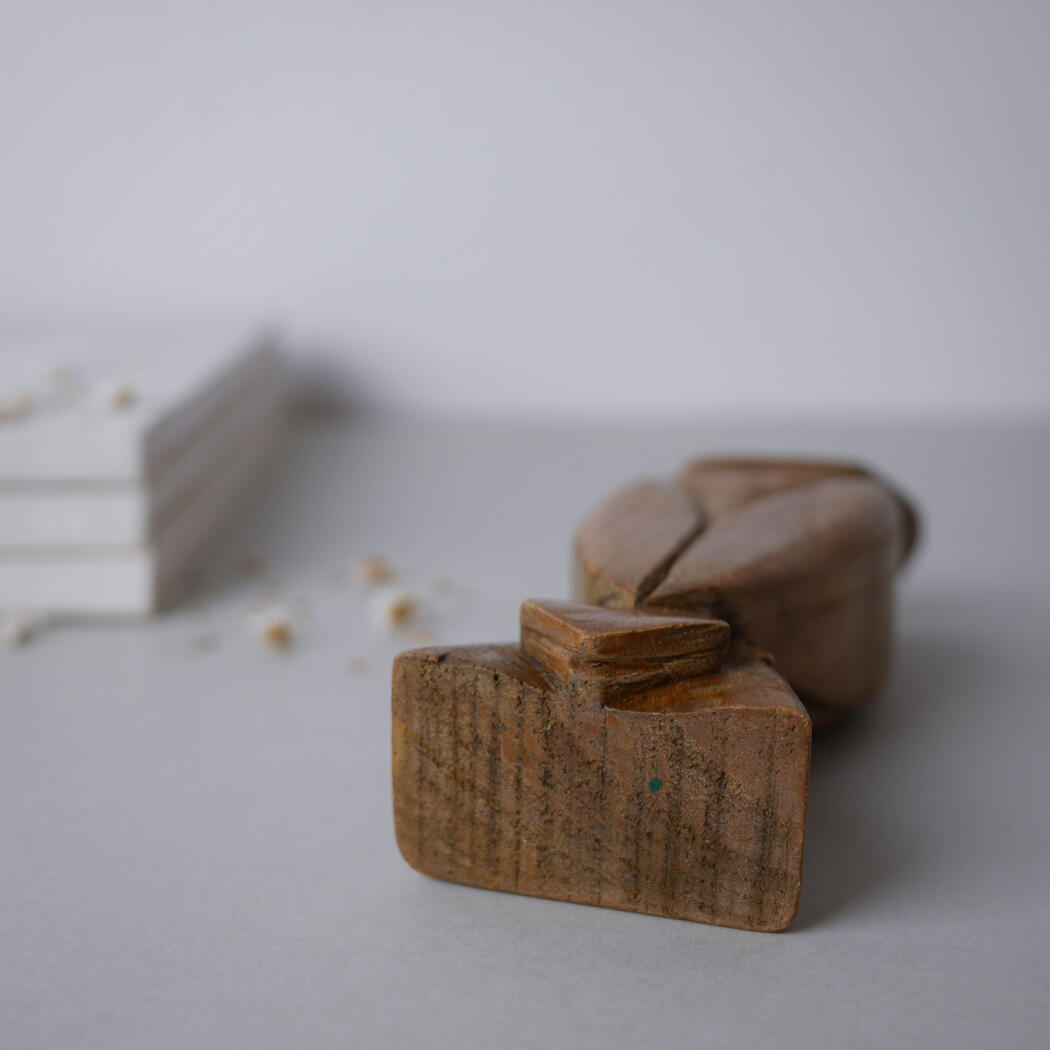 Close-up of a wooden rubber stamp resting on a pale surface with a blurred stack of white books in the background.