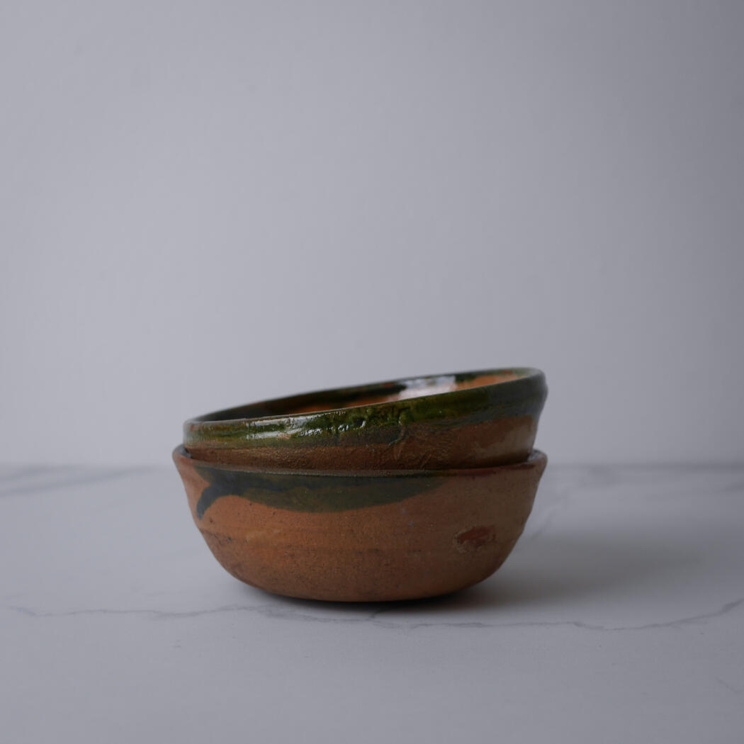 Two handmade ceramic bowls stacked, brown with green glaze, resting on a white marble surface.