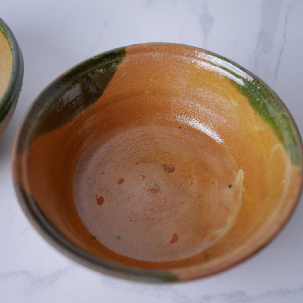 Inside of a glazed ceramic bowl with an orange interior and green rim, viewed from above.