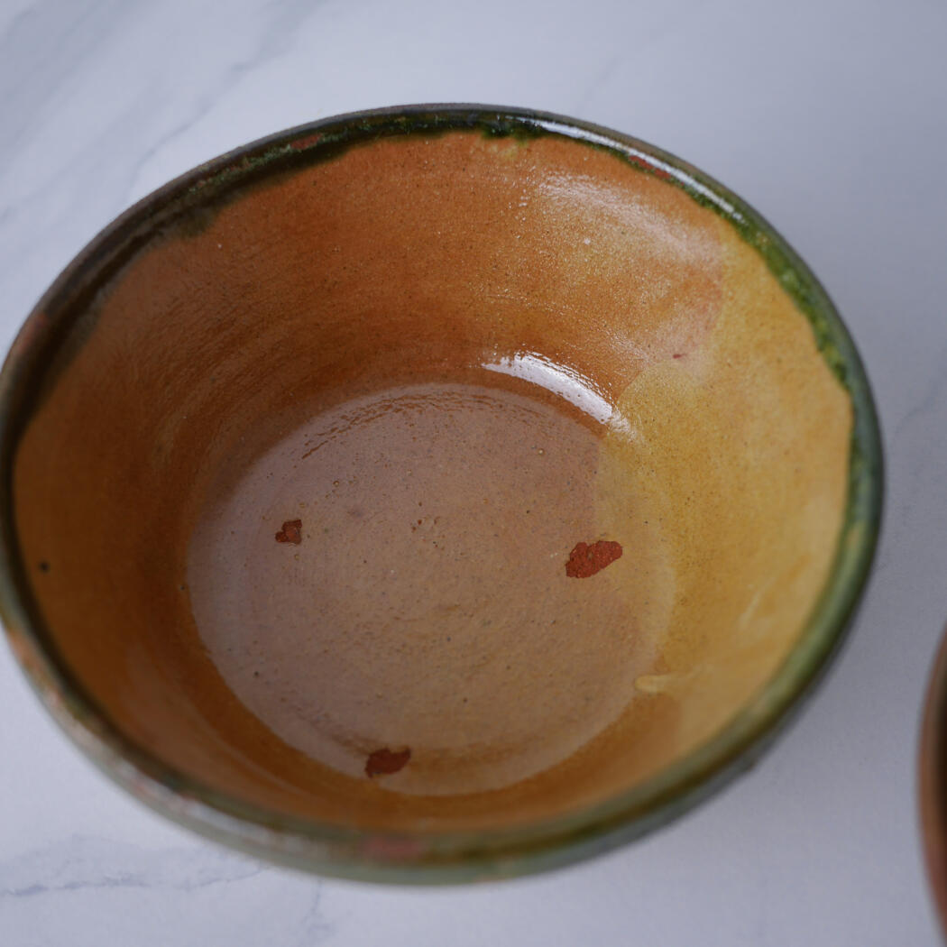 Top-down view of a glazed ceramic mug interior in warm orange-brown glaze with small red glaze spots.