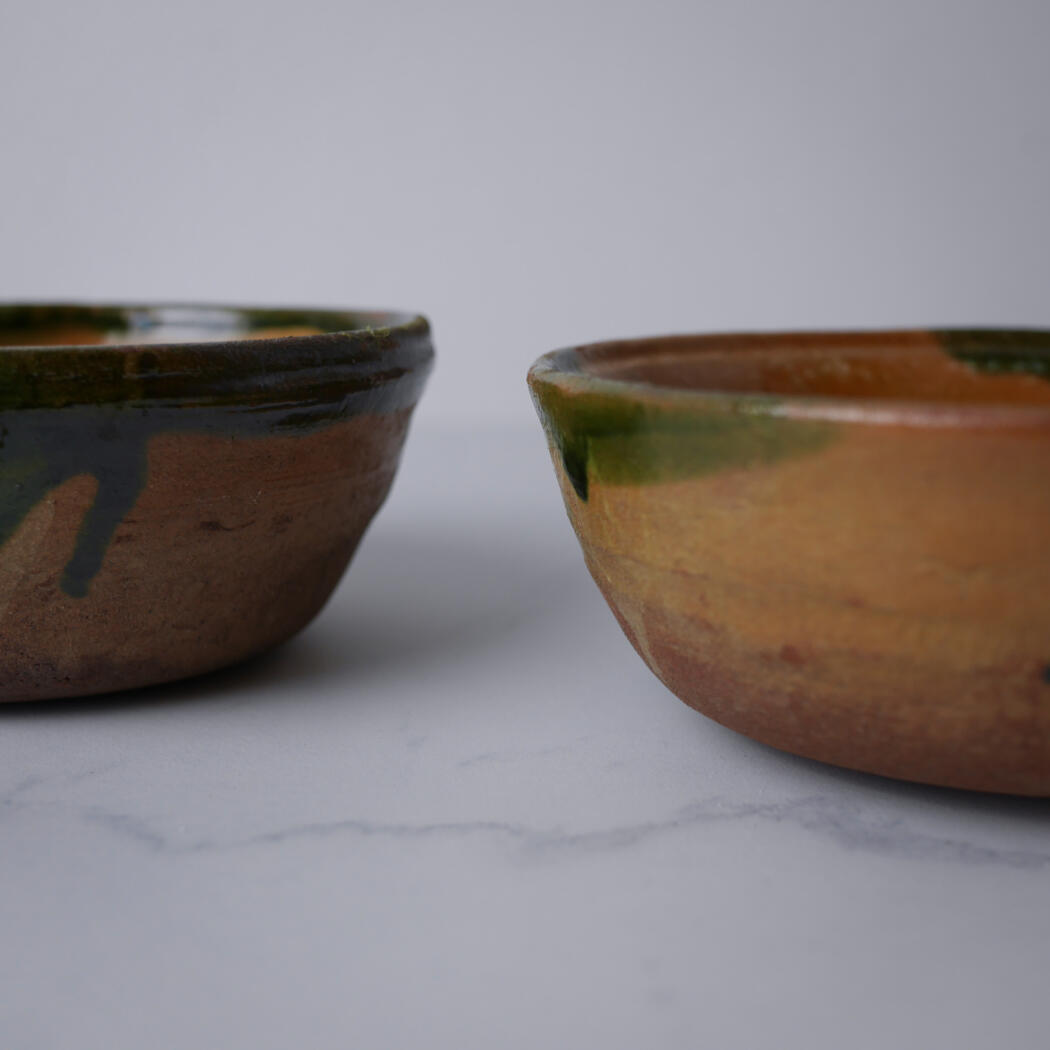 Two rustic ceramic bowls with brown and green glaze sit on a white marble surface.