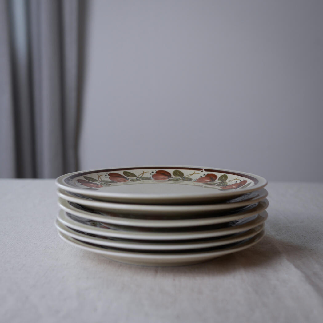 Stack of cream plates with a floral pattern on the top plate, placed on a light table.