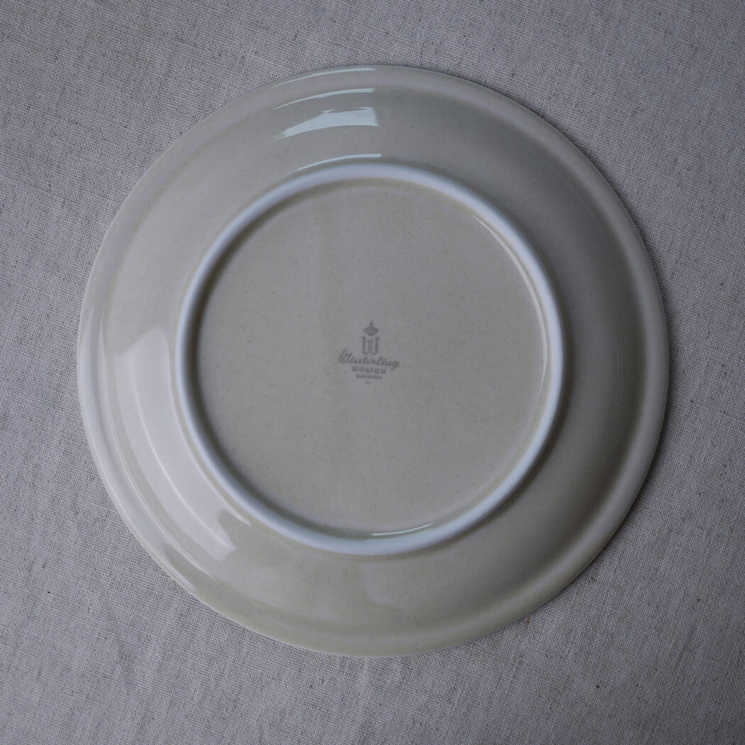 Ceramic plate photographed from above, showing the underside with a faint maker's mark in the center.