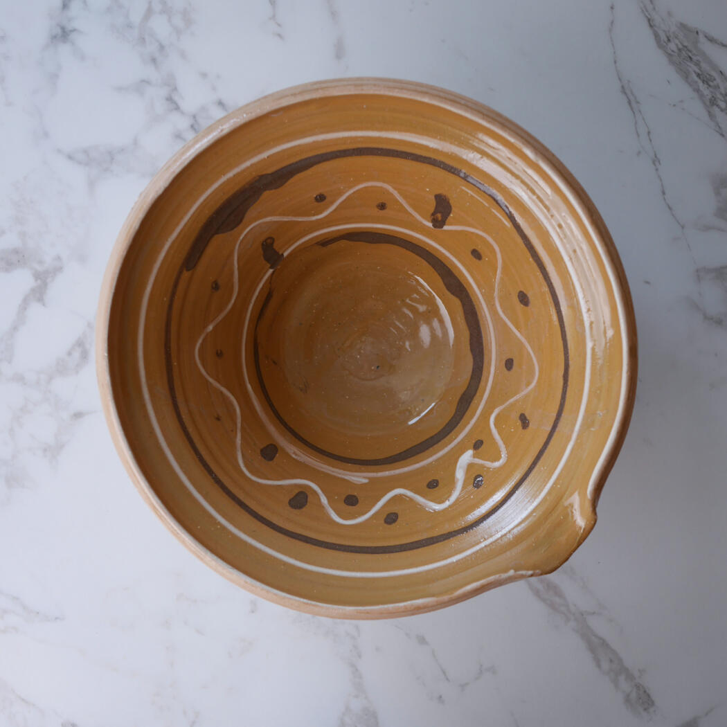 Top-down view of a brown ceramic bowl with white and dark glaze decorations on a marble surface.