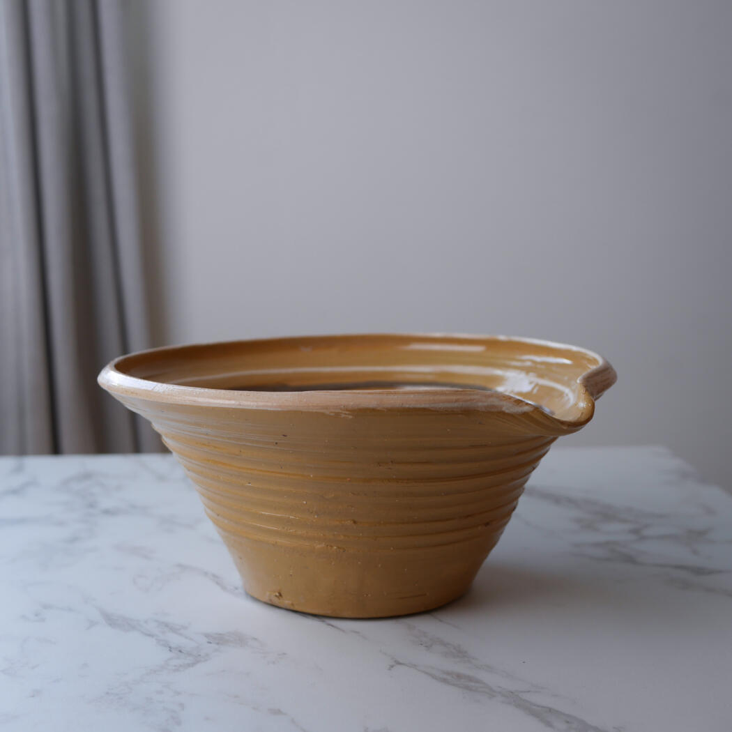 Brown ceramic bowl with a wide, flared rim sits on a white marble table.