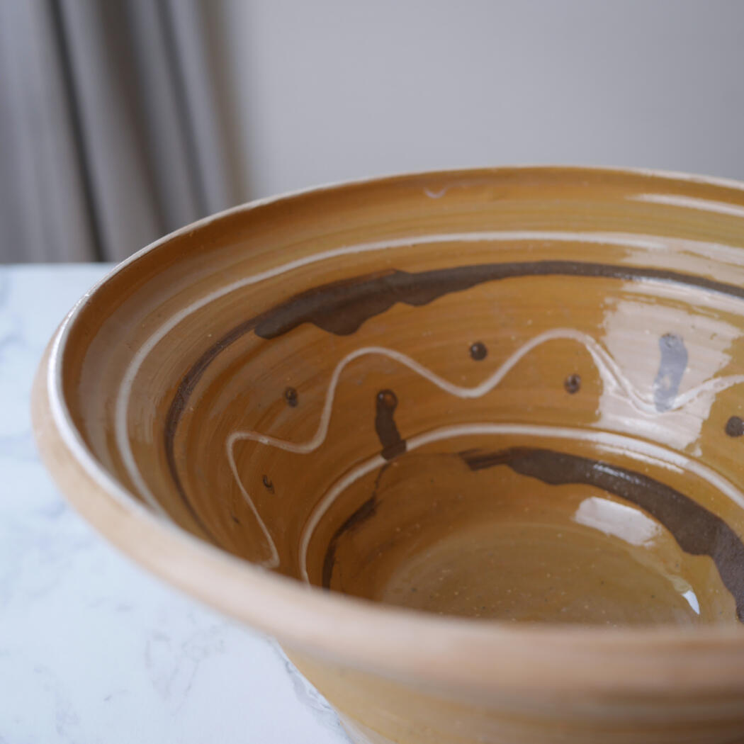 Close-up of a tan ceramic bowl with brown glaze and white decorative lines inside.
