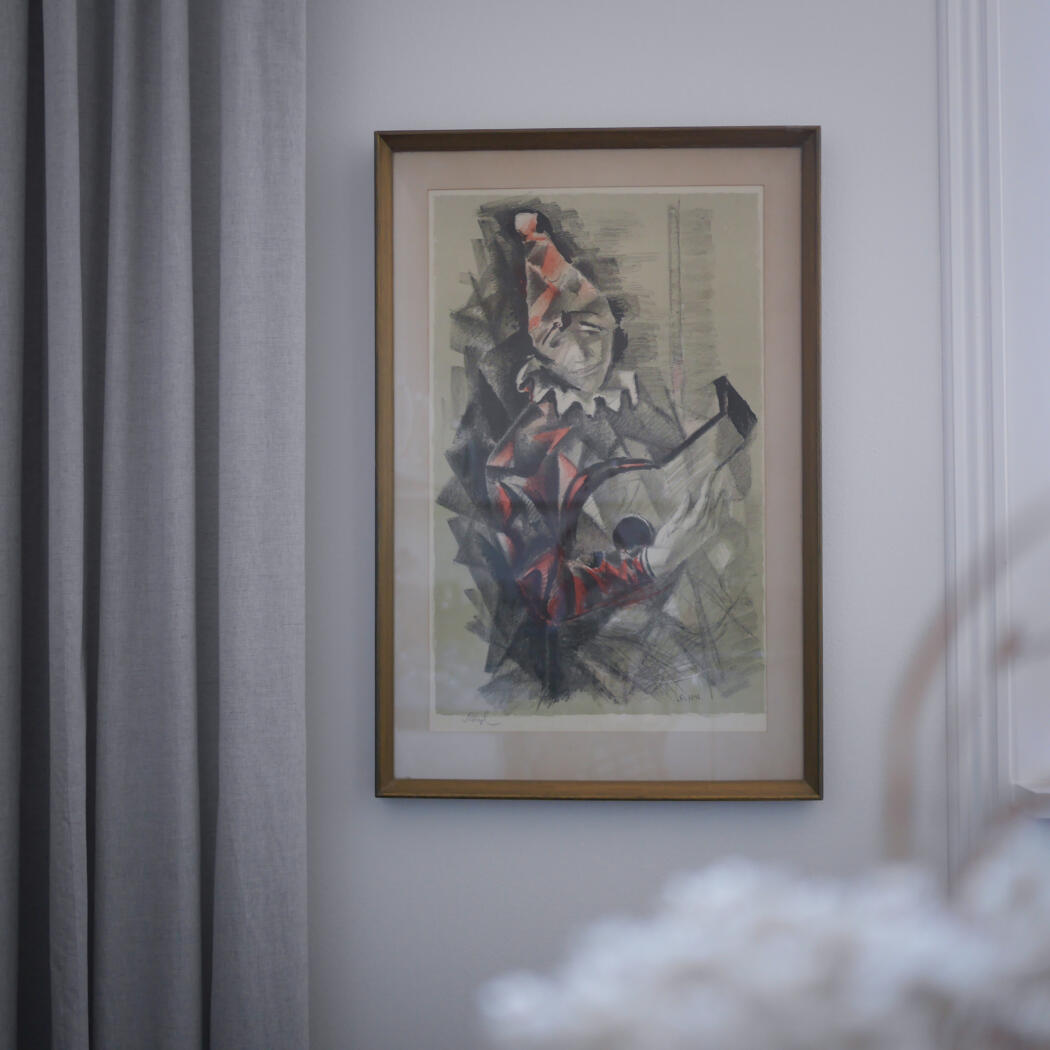 Framed abstract monochrome and red artwork hung on a light gray wall beside curtains, with blurred white flowers in the foreground.”,