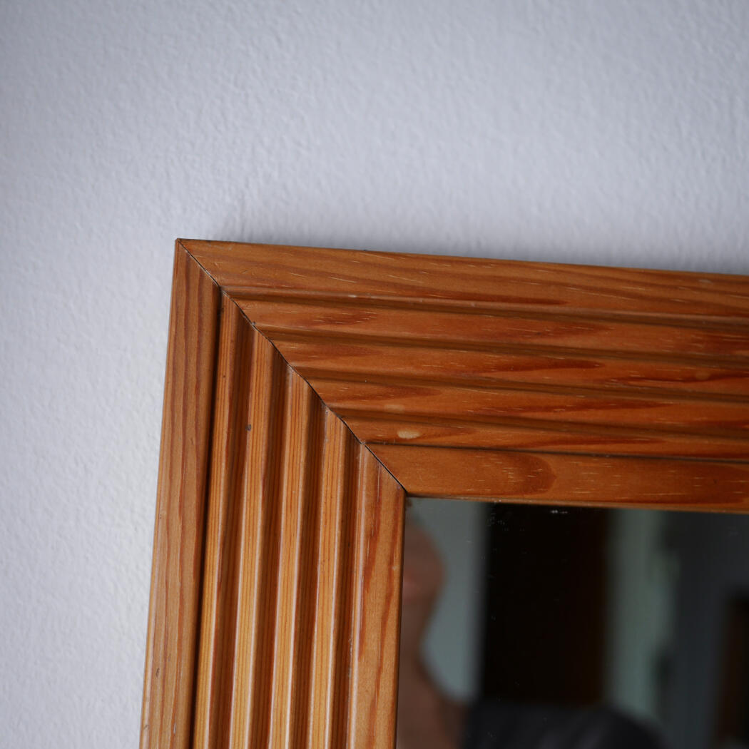 Close-up of a wooden picture frame corner with beveled molding against a light gray wall.