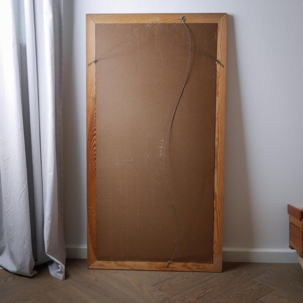 Back of a large wooden-framed canvas leaning against a white wall, with a hanging wire visible at the top and along the back.