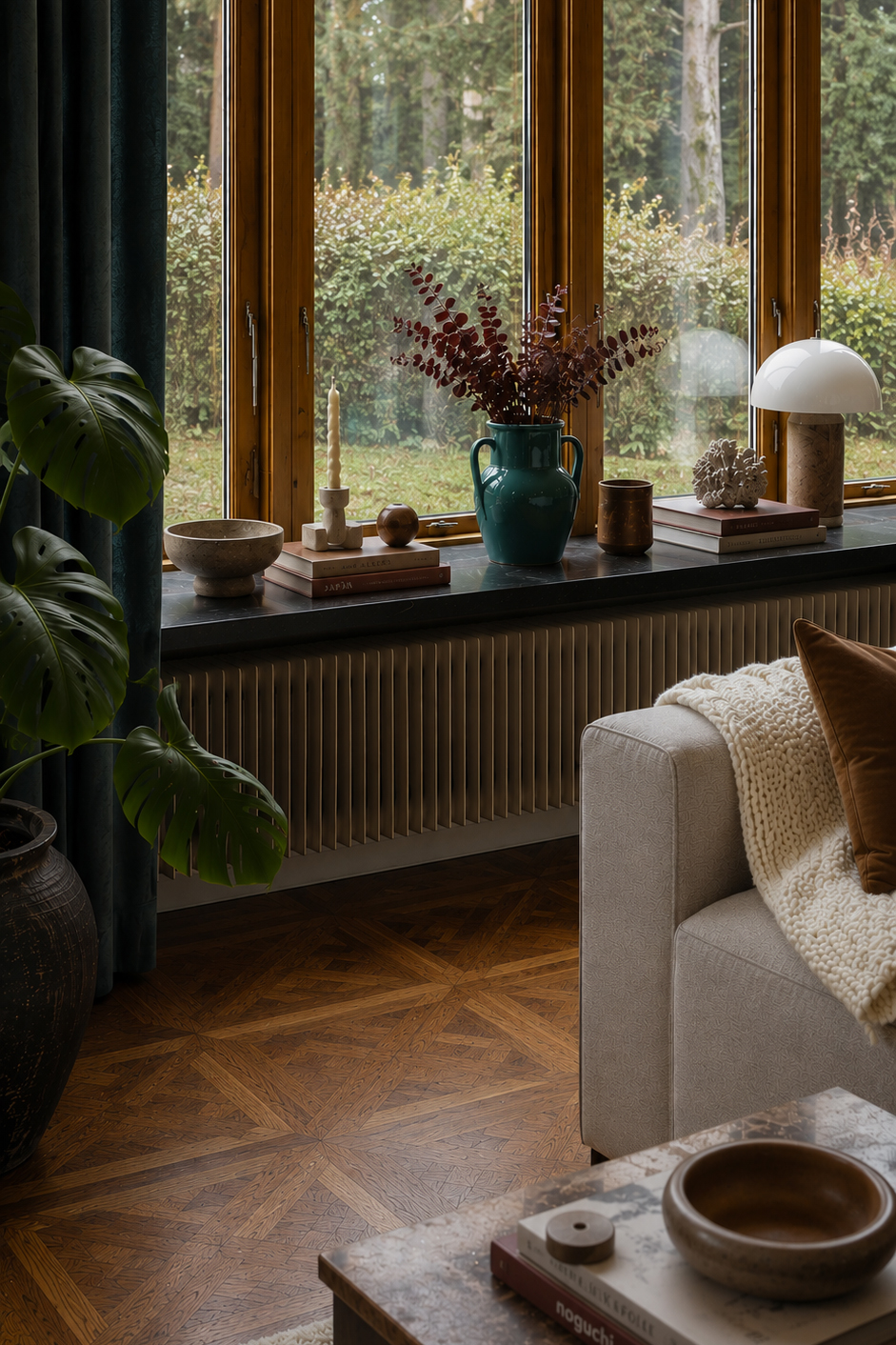 Window sill decor with a teal vase of dried stems, candles, books, and a white arc lamp; beige sofa with chunky knit blanket nearby.